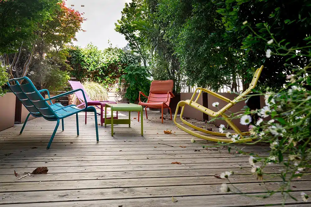 Terrasse bois et son mobilier de jardin coloré entouré d'une végétation généreuse